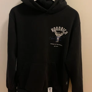 Svart hoodie från Hoodrich - Snygg svart hoodie från Hoodrich med tryck av en ängel på ryggen. Hoodien har en stor ficka fram och textdetaljer på huvan. Den var även en liten ficka på sidan av armen. Köptes 2023, original pris 899. Storlek S kan även passa M. Väldigt skönt material och bekväm.