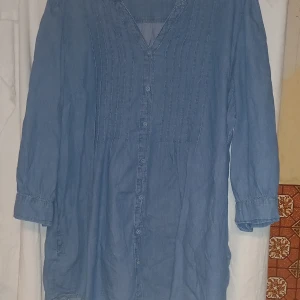 Blå jeansblus el skjorta - Säljer en blå skjorta i 100% bomull med v-ringning och knappar framtill. Skjorta har trekvartsärmar och en avslappnad passform, perfekt för en bekväm stil. Tyvärr finns ingen etikett på storlek. Har testat den och den är alldeles för stor för mig som är storlek M. Antar att de kan va XXL 
