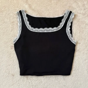 Svart linnetopp med spetsdetaljer - Snygg svart linnetopp med vita spetsdetaljer längs halsringningen och ärmarna. I jättebra skick, strl XS