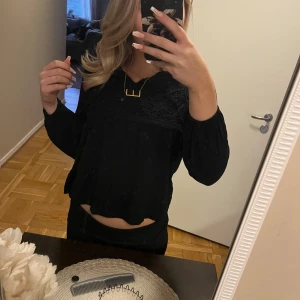 Svart blus med spetsdetaljer - Snygg svart blus med spetsdetaljer på bröstet och långa ärmar. Perfekt för en stilren look. Blusen har en lös passform och en lätt croppad design.