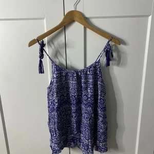 Blåmönstrad linnetopp från KappAhl - Snygg blåmönstrad linnetopp från KappAhl med smala axelband och tofsdetaljer. Perfekt för varma sommardagar.