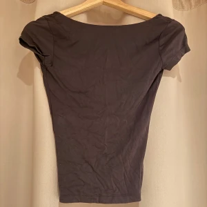 Grå topp från Gina Tricot - Säljer en stilren grå topp från Gina Tricot i storlek XS. Toppen har en djup v-ringning i ryggen och korta ärmar, perfekt för en trendig look.