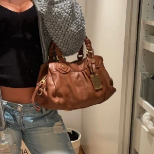 Marc Jacobs Q classic väska - Jättesnygg brun väska av Marc by Marc Jakobs med guld detaljer och äkta läder. I väldigt fint skick, lite slittage på vissa av ”knapparna” men inget som synd vid användning även lite på baksidan- kom privat för fler bilder på det. Lite sminkfläckar på insidan men det går säkert bort med lite varmt vatten. Det långa bandet ingår⭐️⭐️kan gå ner i pris vid snabb affär 