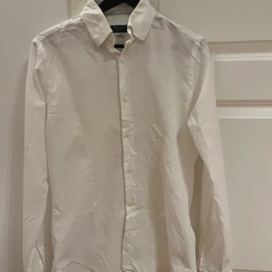 Vit skjorta från ZARA MAN - Klassisk vit skjorta från Eton med långärmad design och knappar framtill. Perfekt för en stilren look. Skjortan är tillverkad i bomull och har en normal passform. Likt en linneskjorta, lite mer genomskinlig. Sommarskjorta