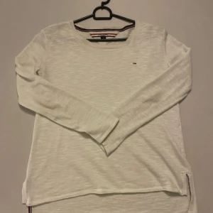 Vit långärmad tröja från Tommy Hilfiger - Säljer en stilren vit långärmad tröja från Tommy Hilfiger. Tröjan har en liten logga på bröstet och ribbade kanter. Perfekt för en avslappnad look.