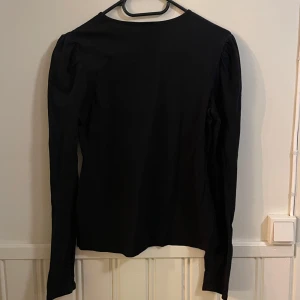 Svart långärmad topp från HM - Snygg svart långärmad topp från HM, med rynkade detaljer vid axlarna. Perfekt för en stilren look. Tillverkad i mjukt bomullsmaterial för extra komfort.