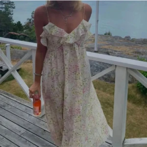 Blommig sommarklänning med volang - Charmig blommig klänning med volangdetaljer och smala axelband. Perfekt för varma sommardagar med sin lätta och luftiga design.