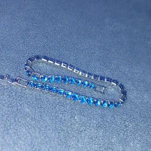 Armband med blå diamanter stenar  - Armband med blå glittriga stenar infattade i en silverfärgad kedja. Cirka 17 cm långt 