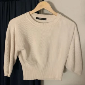 Vit ribbad tröja  - . Tröjan har trekvartsärmar och en rund halsringning, perfekt för en avslappnad look. Passar bra till både jeans och kjol.