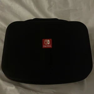 Svart Nintendo Switch väska - Säljer en svart Nintendo Switch väska med röd logotyp. Perfekt för att skydda och transportera din spelkonsol. Väskan har en kompakt design och är lätt att bära med sig. Priset kan diskuteras, och är använd bara cirka 5-10 gånger👍🏼☺️
