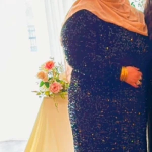 Svart glittrig långklänning - Elegant svart långklänning med glittrande detaljer. Klänningen har långa ärmar och en figurnära passform som ger en sofistikerad look. Perfekt för festliga tillfällen.