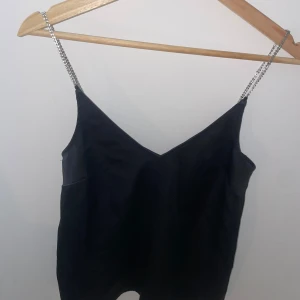 Svart linnetopp med glittriga axelband - Snygg svart linnetopp med glittriga axelband som ger en elegant touch. Perfekt för en kväll ute eller en festlig tillställning. Toppen har en v-ringad design och är tillverkad i ett mjukt material för en bekväm passform🩷🤗