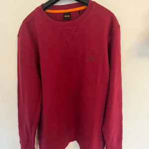 Röd tröja från BOSS - Säljer en stilren röd tröja från BOSS med rund halsringning och diskret logotyp på bröstet. Perfekt för en avslappnad och snygg look. 