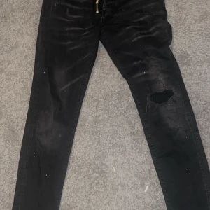 Svarta jeans från Dsquared2 - Snygga svarta jeans från Dsquared2 med en cool slitning på ena benet. De har en dragkedja och knapp framtill samt klassisk femficksdesign. Perfekta för en trendig look.