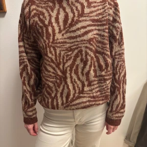 stickad tröja från YAYA - Säljer en snygg brunmönstrad stickad tröja från YAYA. Tröjan har ett zebramönster i burgundy och beige och är långärmad med ribbade muddar. Perfekt för att hålla sig varm och stilren.
