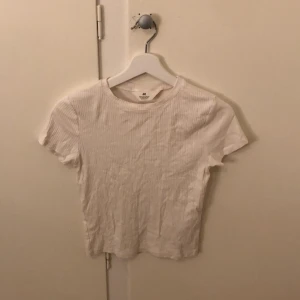 Vit ribbad t-shirt från H&M - Säljer en enkel och stilren vit ribbad t-shirt från H&M. Den har en klassisk rund hals och korta ärmar, perfekt för en avslappnad look.