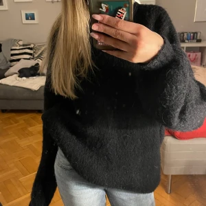 Svart fluffig tröja - Mysig svart tröja i fluffigt material från Vera Moda perfekt för kyliga dagar. Passar bra till både vardag och fest. Ett måste i garderoben för den som älskar komfort och stil! Är i storlek xs men passa upp till m