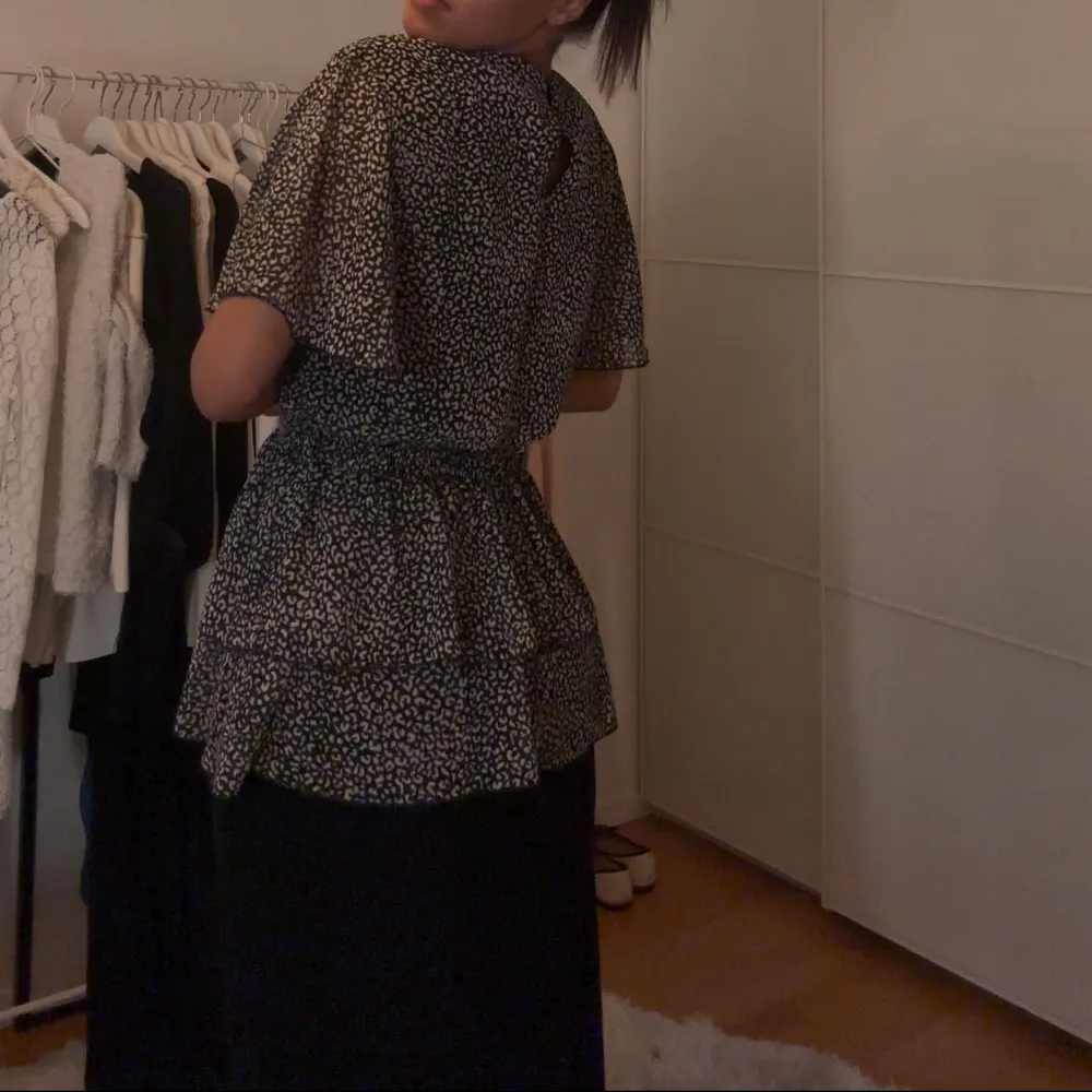 Snygg svart och vit prickig blus med korta ärmar och volangdetaljer. Klänningen har en elastisk midja som ger en fin passform och en luftig känsla. Perfekt för en stilren look.. Puserot.