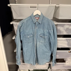 Blå jeansskjorta med fickor - Snygg blå jeansskjorta med klassisk krage och två bröstfickor med knappar. Perfekt för en avslappnad stil. Skjortan har långa ärmar och en rak passform.