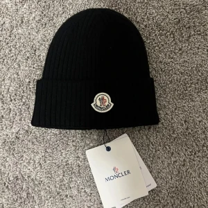 Svart ribbad mössa från Moncler( pris kan diskuteras) - Snygg svart ribbad mössa från Moncler med broderad logotyp framtill. Perfekt för kyliga dagar och en stilren look.