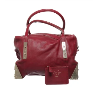 Röd handväska från Adax - Snygg röd handväska i skinn från Adax, designad av Stine Goya. Väskan har metalliska detaljer och en praktisk dragkedja upptill. Perfekt för att ge din outfit en färgklick!