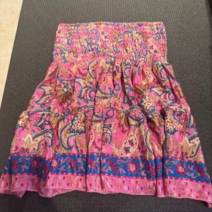 Färgglad kjol i siden och viskos - Säljer en färgglad kjol med ett livfullt mönster i rosa, blått och beige. Kjolen är tillverkad i en mjuk blandning av 70% siden och 30% viskos, vilket ger den ett lyxigt och bekvämt fall. Kjolen är köpt i spanien. Perfekt för att liva upp garderoben! Går också att använda som topp! Eftersom kjolen är i smock passar den från xs-m💞