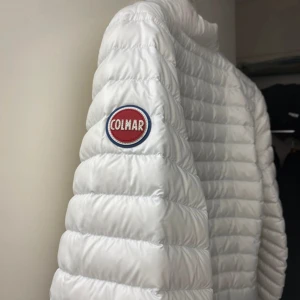 Vit dunjacka från Colmar - Snygg vit dunjacka från Colmar med quiltad design och dragkedja framtill. Jackan har en hög krage och långa ärmar, perfekt för kyligare dagar. Märkeslogga på ärmen och nedre delen av ryggen ger en stilren touch. Använd endast  2-3 gånger⭐️