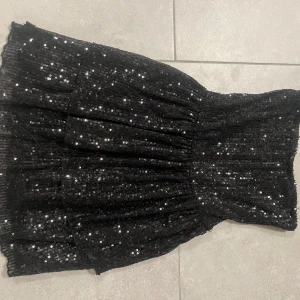 Svart paljettklänning från Gina Tricot - Snygg svart klänning från Gina Tricot täckt med glittriga paljetter. Perfekt för festliga tillfällen med en elegant och iögonfallande design. Axelbandslös modell som ger en stilren look.