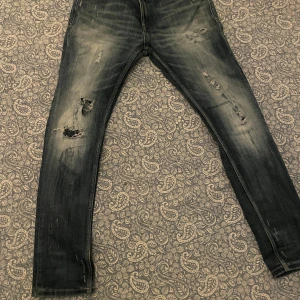 Mörkblåa smog denim  slitna jeans - Snygga svarta jeans med slitningar och en cool tvättad look. Perfekta för en avslappnad stil. De har en klassisk femficksdesign och dragkedja.