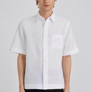 Filippa k vit kortärmad skjorta - Säljer en stilren vit kortärmad skjorta med knappar och en bröstficka. Perfekt för varma dagar och en avslappnad look.