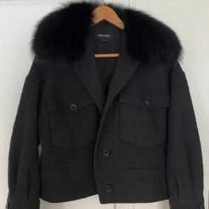 Meotine Charlie jacket  - Snygg svart jacka från Meotine med en lyxig pälsdetalj runt kragen. Jackan har knappar framtill och två stora fickor på bröstet. Perfekt för kyligare dagar när du vill hålla stilen.