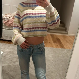 Randig croppad tröja från Pull&Bear - Säljer en mysig croppad tröja från Pull&Bear med färgglada ränder i blått, rosa och grönt. Tröjan har långa ärmar och en bekväm passform. Perfekt för en avslappnad stil!