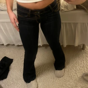 Mörkblå bootcut jeans lågmidjade  - Snygga mörkblå bootcut jeans med låg midja och kontrasterande sömmar. Perfekta för en avslappnad stil. De har klassisk femficksdesign och en bekväm passform.