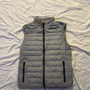 Grå dunväst från Duno - Grå dunväst från Duno. Ganska lightweight, och sjukt skön. Västen är i bra skick. Man kan även packa ner västen till en liten väska via en ficka på innersidan. Nypris 3500:-
