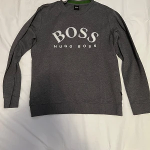 Grå Hugo Boss Sweatshirt Storlek Large  - En grå Hugo boss sweatshirt med vitt tryck på bröstet som är i storlek large, sweatshirten är i bra skick. Tveka inte på att höra av dig om du är intresserad eller om du har några frågor!