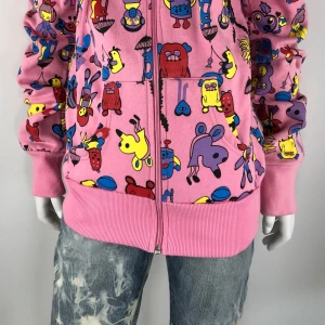 Färgglad hoodie med tecknat mönster - Säljer en färgglad hoodie med dragkedja och tecknat mönster i olika färger. Basen är rosa med figurer i blått, gult och rött. Perfekt för dig som vill sticka ut med en unik stil!