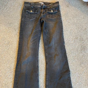 Svarta jeans med fickdetaljer - Snygga svarta jeans med raka ben och dekorativa fickor med knappar bak. Perfekta för en avslappnad stil. Klassisk design med dragkedja och knapp framtill.