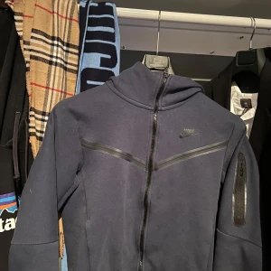 Mörkblå hoodie från Nike - Hej, säljer denna Nike tech tröjan, den är i storlek S och är i fint skick, vid frågor intresse eller någon annan fundering är det bara höra av dig!!