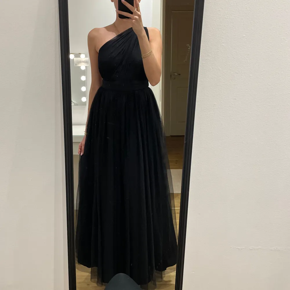 Elegant svart långklänning med oneshoulder-design och öppen rygg. Perfekt för formella tillfällen med sin flytande siluett och stilrena look.. Mekot.