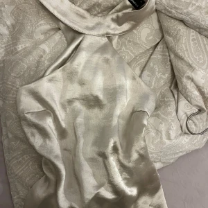 Champagnefärgad topp från Gina Tricot - Elegant champagnefärgad topp från Gina Tricot i ett glansigt material. Toppen har en hög krage och är ärmlös, vilket ger en stilren look. Perfekt för speciella tillfällen.