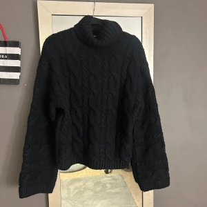 Svart stickad polotröja från Bik Bok - Mysig svart stickad polotröja från Bik Bok i storlek XS. Tröjan har ett klassiskt flätmönster och långa ärmar, perfekt för kyliga dagar. Den höga kragen ger extra värme och stil. Säljer tröjan pågrund av att den ej kommer till användning nåmer. Nypris 400kr