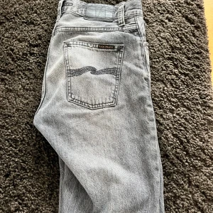 Grå jeans från Nudie Jeans - Snygga grå jeans från Nudie Jeans med otroligt bra skick med klassisk femficksdesign och subtila slitningar. De har en rak passform. Tillverkade i högkvalitativt denim för en bekväm känsla.