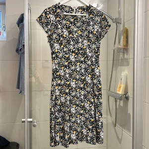 Blommig klänning från Object - Säljer en söt blommig klänning från Object. Den har en svart bas med vita och gula blommor. Klänningen är kortärmad och har en rund halsringning. Perfekt för vår och sommar!