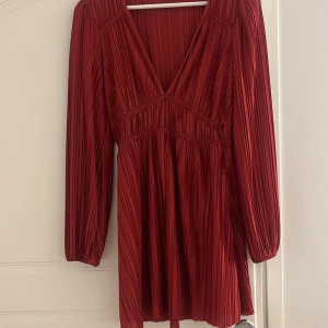 Röd klänning från Zara - Snygg röd klänning från Zara med v-ringning och långa ärmar. Den har ett plisserat mönster som ger en elegant touch. Perfekt för höst och vinter💕