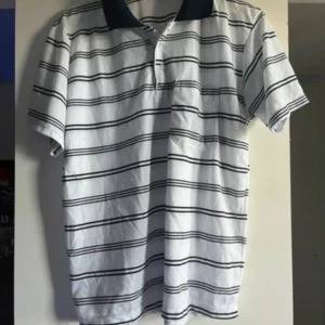 Vit och svart randig pikétröja från & Other Stories - Säljer en tunn och stilren vit pikétröja med svarta ränder från & Other Stories. Tröjan har korta ärmar och en klassisk krage. Perfekt för en avslappnad och snygg look.