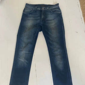 Blå jeans från Nudie Jeans - Snygga blå jeans från Nudie Jeans med en klassisk femficksdesign. De har en slimfit / regular passform och är tillverkade i slitstarkt denim. Perfekta för en avslappnad stil.