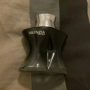 Herrparfym från Silenzia - Säljer en elegant och maskulin parfym från Silenzia för män. Flaskan är svart med en stilren, kurvig design och har en silverfärgad kork. Knappt använd! Luktar väldigt gott och fräscht 