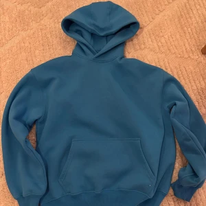 Oversized Blå hoodie - Säljer en snygg blå oversized hoodie med en stor ficka framtill och en bekväm huva. Knappt använd så den är som ny. 