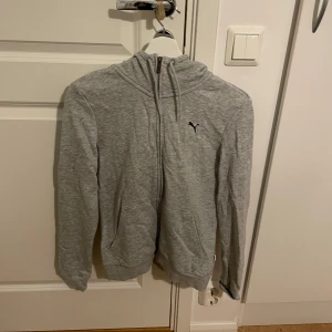 Grå hoodie från Puma - Säljer en stilren grå hoodie från Puma med dragkedja och huva. Perfekt för en avslappnad look. Den har långa ärmar och en liten Puma-logga på bröstet. Passar bra till både jeans och träningsbyxor. För fler frågor och bilder kan man kontakta mig privat🤍