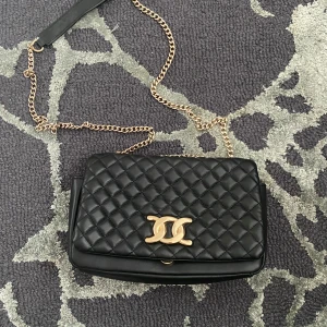 Svart handväska - Fin svart handväska med guldfärgat band. Väskan har en praktisk dragkedja inuti för säker förvaring. 💞